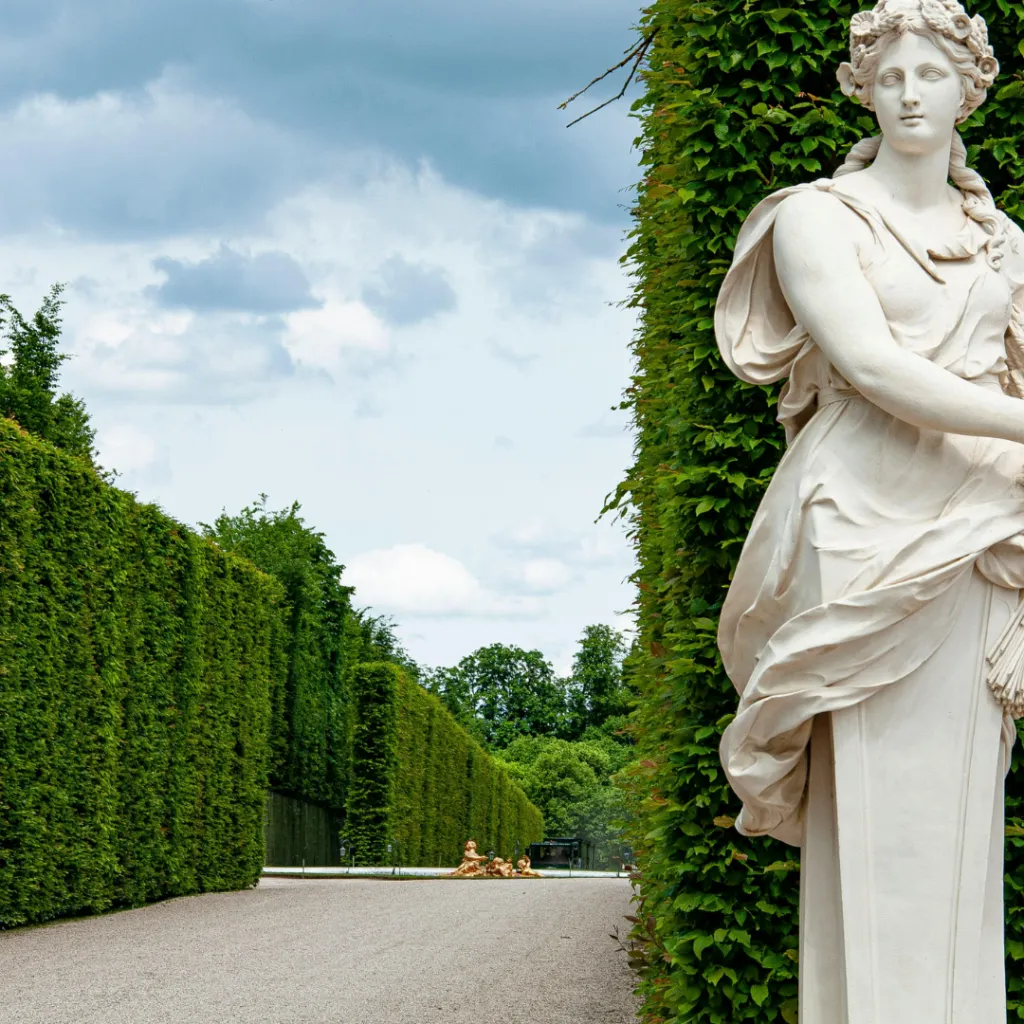 Statue classique apparaissant au bord d’une allée végétale